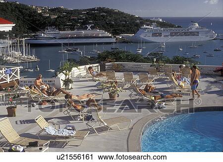 Stock Image -  U. S. Virgin Islands, St. Thomas, Caribbean, USVI, U. S. V. I Virgin Islands, cruise, pool, People sunbathing next to swimming pool at Bluebeards Castle and scenic view of cruise ships in the harbor in Charlotte Amalie the territorial capital of the US Virgi. Fotosearch