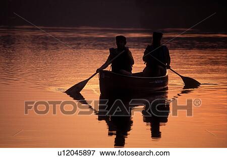 Stock Photo -  Vermont, canoe, canoeing, Mother and daughter paddle a canoe over the quiet calm waters of Kettle Pond at[sunrise, sunset] in Groton State Forest. Mad River Canoe Products.. Fotosearch