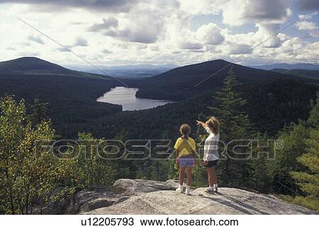 Stock Image -  Vermont, Mother and daughter standing on Owl's Head Overlook looking down on Kettle Pond in Groton State Forest in Caledonia County in the state of Vermont. Mother pointing her finger showing something to daughter. . Fotosearch