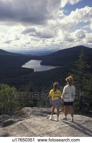 Stock Image -  Vermont, Mother and daughter standing holding hands on Owl's Head Overlook looking down on Kettle Pond in Groton State Forest in Caledonia County in the state of Vermont. . Fotosearch