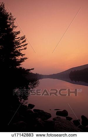 Stock Image -  Vermont, [Sunrise, sunset] over quiet calm Kettle Pond in Groton State Forest . Fotosearch
