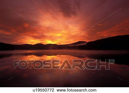 Stock Image -  Vermont, The colorful [sunrise, sunset] reflects over the quiet calm waters of Mollys Falls Pond in the early morning in Cabot . Fotosearch