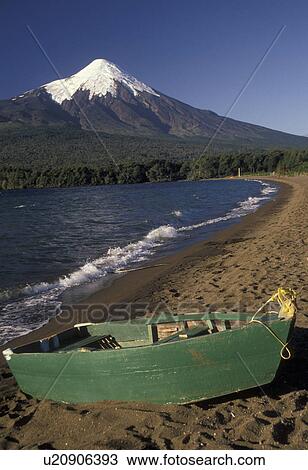Stock Image -  volcano, Chile, Mt. Osorno, Andes, Scenic view of the snow capped Osorno Volcano from Lago Llanquihue in the South-Central Region (the Land of Lakes and Volcanoes) in Chile. A green rowboat is rests on the sandy beach of the lake in the foreground.. Fotosearch