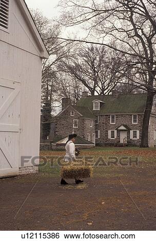 Stock Photograph -  Washington Crossing, Pennsylvania, Interpreter at Washington Crossing Historic Park carries a bale of straw out of the barn in the state of Pennsylvania . Fotosearch