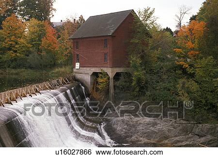 Stock Photograph -  waterfall, dam, Vermont, Morrisville, Lamoille River, Scenic waterfall running over a dam next to a red wooden house in the fall.. Fotosearch