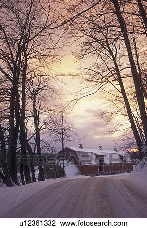 Stock Image -  winter scene, country road, sunset, Vermont, Snow covered country road at sunset with a red barn in the distance on a winter day in Cambridge in Lamoille County in the state of Vermont. . Fotosearch