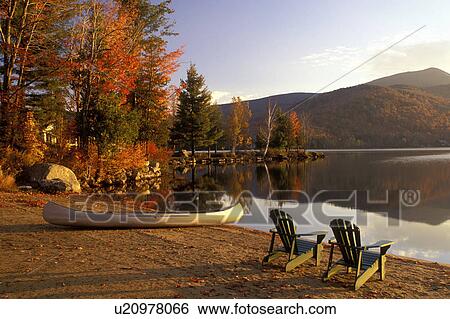 Stock Photograph -  Adirondack chairs, lake, canoe, Adirondacks, New York, Blue Mountain Lake, NY, A canoe and two Adirondack chairs on a quiet beach on the calm waters of Blue Mountain Lake in the autumn in the Adirondacks.. Fotosearch