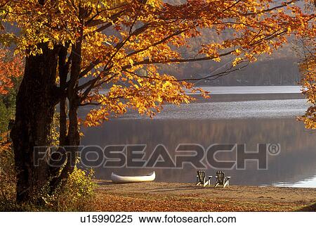 Stock Photography -  Adirondacks, canoe, chairs, New York, Blue Mountain Lake, NY, Two Adirondack chairs and a canoe on a quiet beach on Blue Mountain Lake in the autumn in the Adirondacks.. Fotosearch