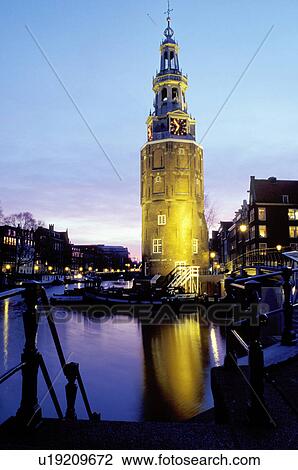 Stock Image -  Amsterdam, clock tower, canal, Holland, The Netherlands, Europe, The illuminated clock tower reflects in the calm waters of the canal (grachten) in downtown Amsterdam at night . Fotosearch