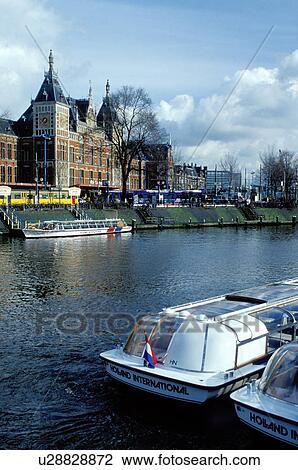 Amsterdam, Holland, The Netherlands, Europe, Tour boats along a canal in front of Central Station in Amsterdam. View Large Photo Image Stock Image - Amsterdam, Holland, The Netherlands, Europe, Tour boats along a canal in front of Central Station in Amsterdam. . Fotosearch