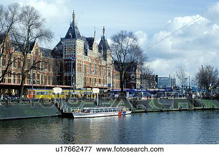 Stock Photo -  Amsterdam, The Netherlands, Holland, Europe, Tour boat along a canal in front of Central Station in Amsterdam. . Fotosearch