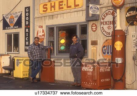 Stock Photo -  antique, gas station, collectibles, Father and son stand in front of a collection of old signs and other memorabilia on Steve Morris Garage and Auto Sales in Orange in Orange County in the state of Vermont.. Fotosearch