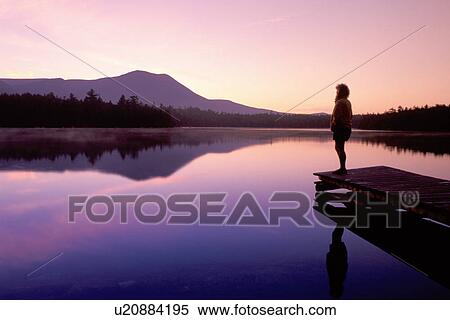 Stock Photography -  Baxter Park, Maine, sunrise, sunset, ME, Silhouette of a woman standing on a dock looking at Mt. Katahdin reflecting in the calm waters of Daicey Pond at sunrise in Baxter State Park. . Fotosearch