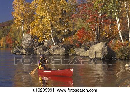 Stock Image -  canoe, canoeing, autumn, VT, Vermont, Woman paddling a red canoe along the rocky shoreline of Lake Groton in Groton State Forest in the fall.. Fotosearch