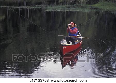 Stock Photo -  canoeing, canoe, photography, Vermont, VT, Woman taking a picture from a red canoe on Green River Reservoir in Hyde Park. . Fotosearch