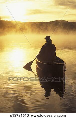 Stock Image -  canoeing, canoe, sunrise, sunset, Vermont, VT, Woman canoeing on Mollys Falls Pond in the fog.. Fotosearch