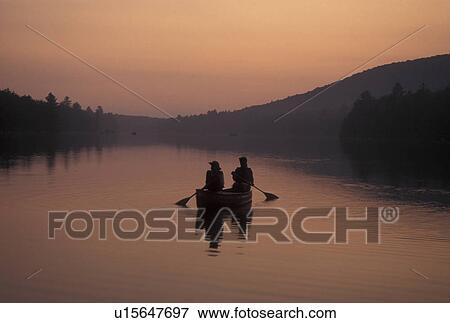 Stock Photo -  canoeing, canoe, sunset, sunrise, Vermont, VT, Mother and daughter paddle a canoe at sunset on Kettle Pond in Groton State Forest.. Fotosearch
