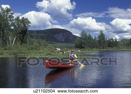 Picture -  canoeing, canoe, Vermont, VT, Woman paddling a red canoe on Marshfield Pond in Marshfield. blue sky and puffy clouds.. Fotosearch
