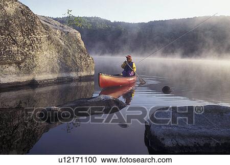 Stock Image -  canoeing, canoe, Vermont, VT, Woman paddles a canoe on Kettle Pond through boulders in the mist in Groton State Forest.. Fotosearch