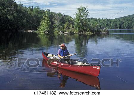 Stock Image -  canoeing, canoe, Vermont, VT, Woman paddling a red canoe on Green River Reservoir in Hyde Park. . Fotosearch