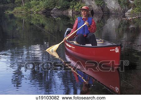 Stock Image -  canoeing, canoe, Vermont, VT, Woman paddling a red canoe on Green River Reservoir in Hyde Park. . Fotosearch