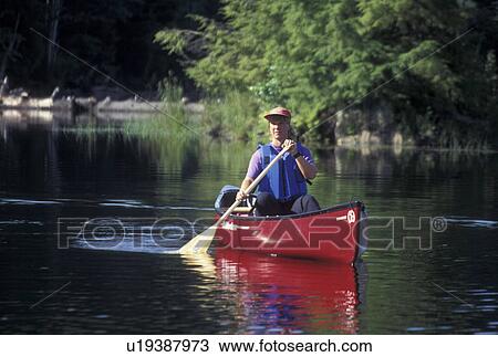 Stock Image -  canoeing, canoe, Vermont, VT, Woman paddling a red canoe on Green River Reservoir in Hyde Park. . Fotosearch