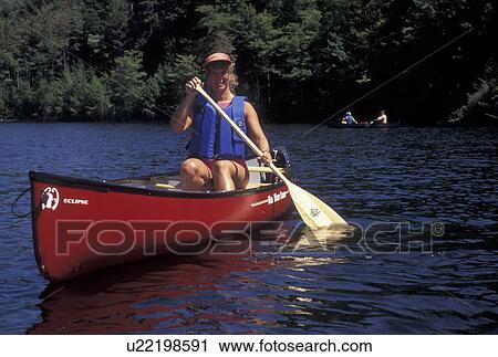 Stock Image -  canoeing, canoe, Vermont, VT, Woman paddling a red canoe on Green River Reservoir in Hyde Park. . Fotosearch