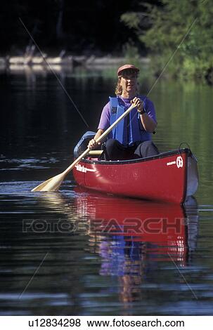 Stock Photo -  canoeing, canoe, Vermont, VT, Woman paddling a red canoe on Green River Reservoir in Hyde Park. . Fotosearch