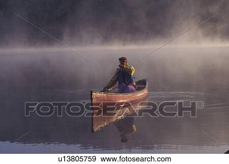 Stock Photo -  canoeing, canoe, Vermont, VT, Woman paddling a red canoe on Kettle Pond in the fog in Groton State Forest.. Fotosearch