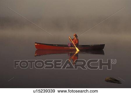 Stock Photo -  canoeing, canoe, Vermont, VT, Woman paddling a red canoe on Mollys Falls Pond at sunrise in the fog.. Fotosearch