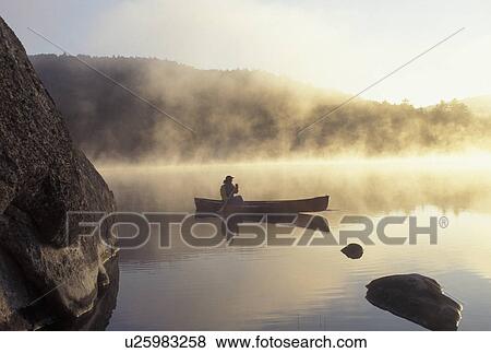 Stock Photo -  canoeing, canoe, Vermont, VT, Woman paddles a canoe on Kettle Pond in the mist in Groton State Forest.. Fotosearch