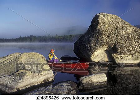 Stock Photograph -  canoeing, canoe, Vermont, VT, Woman paddling a red canoe on Kettle Pond through boulders in the mist in Groton State Forest.. Fotosearch