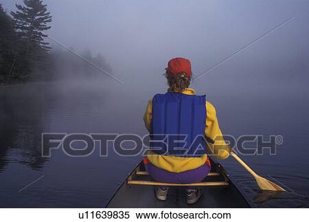 Stock Photography -  canoeing, canoe, Vermont, VT, Woman paddling a canoe on Kettle Pond in the fog in Groton State Forest.. Fotosearch