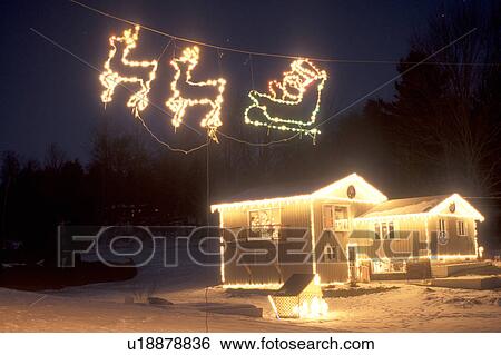 Stock Photograph -  Christmas, decorations, home, holiday, snow, winter, A house is trimmed with lights as an illuminated Santa's sleigh pulled by reindeer flies through the air for Christmas holiday season in East Montpelier at night in Washington County in the state of Ve. Fotosearch
