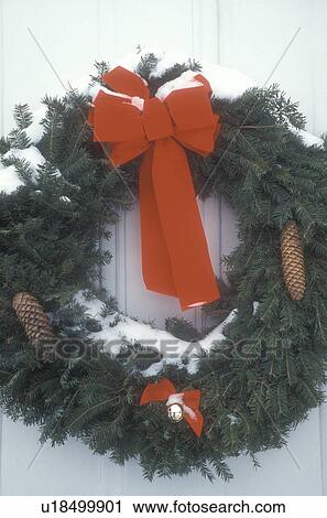 Stock Image -  Christmas wreath, ribbon, red bow, wreaths, close-up, decoration, Christmas, holiday, snow, winter, A snow covered green wreath with red bows and pine cones decorate the outside door of a house in the state of Vermont. . Fotosearch