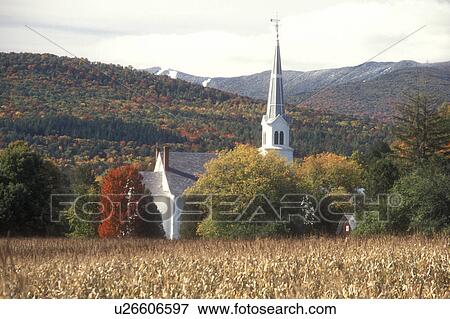 Stock Photo -  church, fall, Waitsfield, VT, Vermont, Scenic view of the United Church of Christ surrounded by colorful fall foliage from a cornfield with the first snow on the Green Mountains and the slopes of Sugarbush Ski Resort in the background in autumn.. Fotosearch