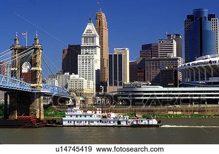 Stock Photo -  Cincinnati, skyline, OH, Ohio, Downtown skyline of Cincinnati. Barge chugs along the Ohio River.. Fotosearch