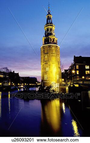 Stock Image -  clock tower, canal, Amsterdam, The Netherlands, Holland, Europe, The illuminated clock tower reflects in the calm waters of the canal (grachten) in downtown Amsterdam at night. Fotosearch