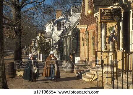 Picture -  Colonial Williamsburg, Virginia, VA, Williamsburg, Interpreters wearing colonial costumes walk down the sidewalk outside the village stores in Colonial Williamsburg.. Fotosearch