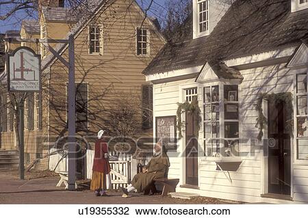Stock Image -  Colonial Williamsburg, Virginia, VA, Williamsburg, Interpreters wearing colonial costumes talk outside the village post office in Colonial Williamsburg.. Fotosearch