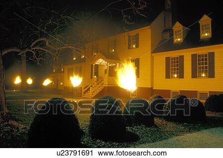 Stock Image -  Colonial Williamsburg, Virginia, VA, Williamsburg, Illumination at Christmas in the evening in Colonial Williamsburg. Flickering cresset lights guide visitors through tours of historic buildings.. Fotosearch