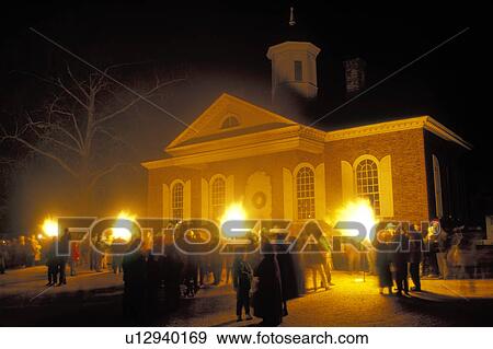 Stock Photo -  Colonial Williamsburg, Virginia, VA, Williamsburg, Illumination of Market Square at Christmas in front of the Courthouse in the evening in Colonial Williamsburg. Flickering cresset lights guide visitors through tours of historic buildings.. Fotosearch