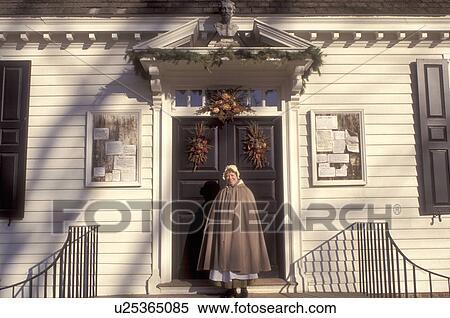 Stock Photography -  Colonial Williamsburg, Virginia, VA, Williamsburg, Interpreter wearing colonial costume stands outside the village store in Colonial Williamsburg.. Fotosearch