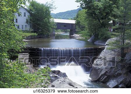 Stock Photo -  covered bridge, waterfall, dam, spring, Warren, VT, Vermont, Warren Covered Bridge crosses the Mad River with a waterfall in the foreground in Warren in the Mad River Valley in the spring. . Fotosearch