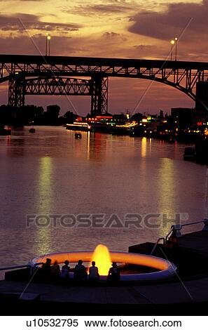 Stock Photography -  fountain, bridge, Cleveland, OH, Ohio, Flats District, Fountain at Settlers Landing Park along the Cuyahoga River in the Flats District of downtown Cleveland illuminated at night. Main Avenue Bridge crossing the Cuyahoga River in the background.. Fotosearch