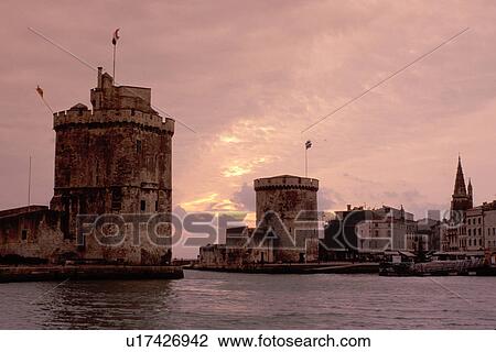 Stock Image -  France, La Rochelle, Poitou-Charentes, Charente-Maritime, Europe, 14th century medieval stone towers at the entrance to the harbor of the ancient fortified old port city of La Rochelle at sunset on the Atlantic Ocean.. Fotosearch