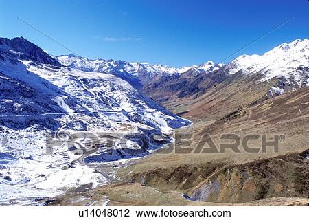 Stock Image -  France, Midi-Pyrenees, Col du Tourmalet, The Pyrenees, Hautes-Pyrenees, Europe, A mountain road winds down through the snow capped Pyrenees Mountains and the valley below of Col du Tourmalet.. Fotosearch