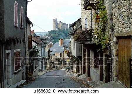 Stock Image -  France, the Dordogne, Quercy, Midi-Pyrenees, Najac, Aveyron, Europe, A narrow street runs through the medieval hilltop village of Najac. A castle sits on top of the hill in the distance.. Fotosearch