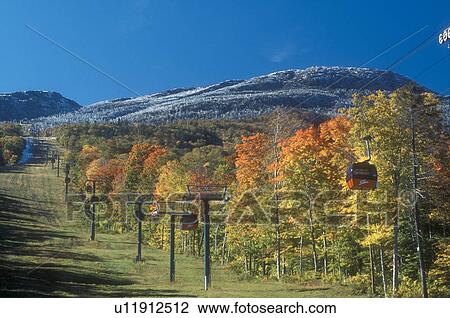Stock Image -  gondola, fall, Stowe, VT, Vermont, Mount Mansfield, Red gondolas at Stowe Mountain Resort go up to Mt. Mansfield with its first dusting of snow surrounded by colorful fall foliage in autumn. . Fotosearch