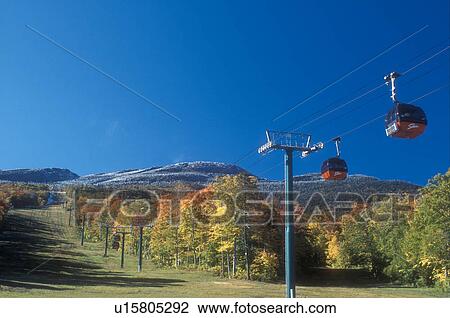 Stock Image -  gondola, fall, Stowe, VT, Vermont, Mount Mansfield, Red gondolas at Stowe Mountain Resort go up to Mt. Mansfield with its first dusting of snow surrounded by colorful fall foliage in autumn. . Fotosearch